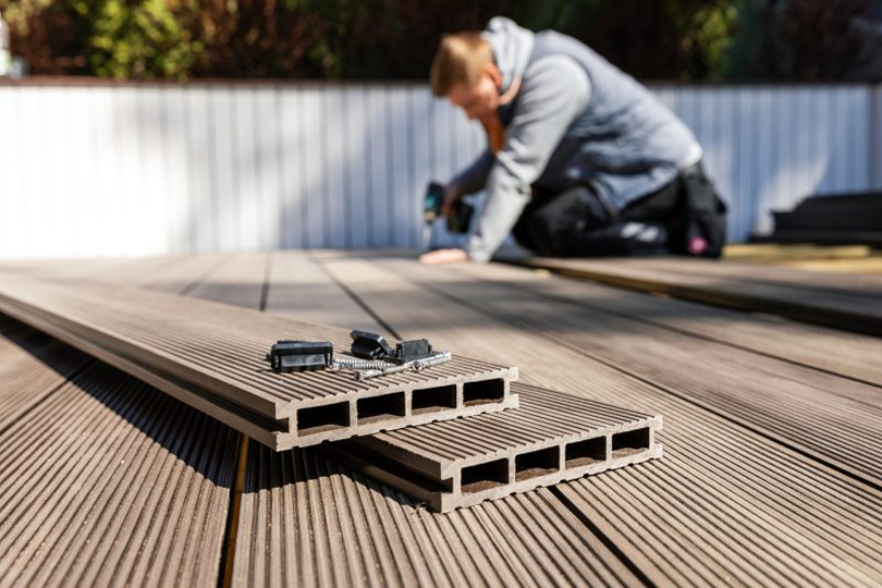 Person installing composite decking boards with tools and fasteners placed on the deck surface.