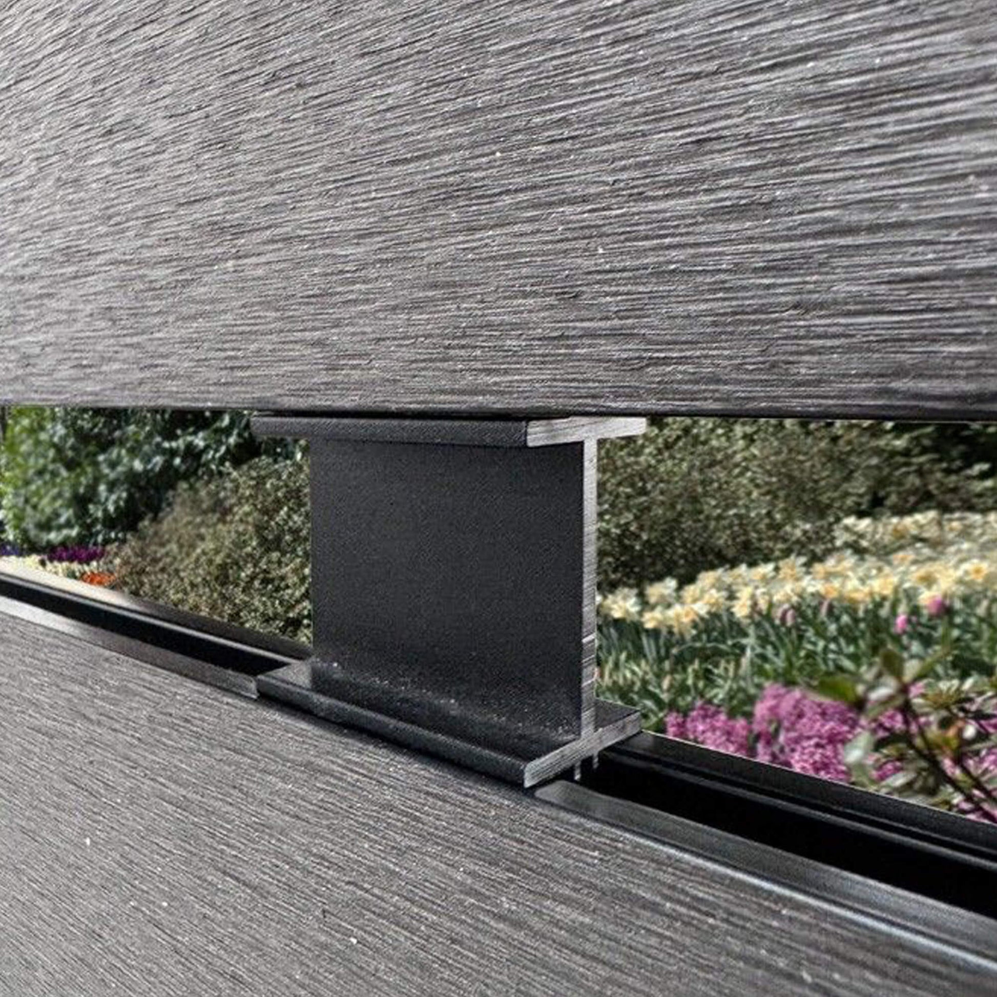 Charcoal Aluminium Spacer in situ between two Charcoal Composite Fence Slat with a garden background.