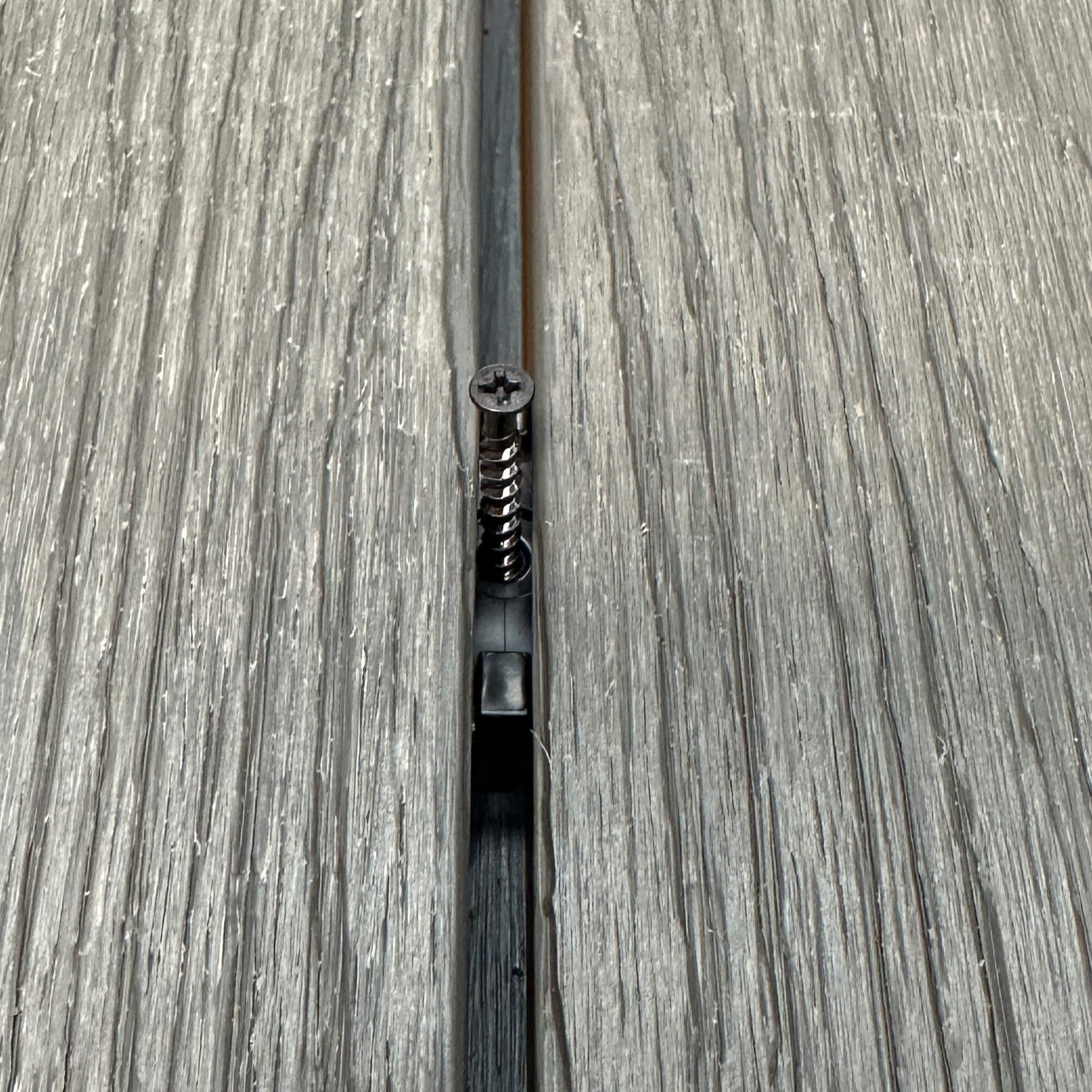 A Black Decking Clip & Screw in situ on a decking patio background.