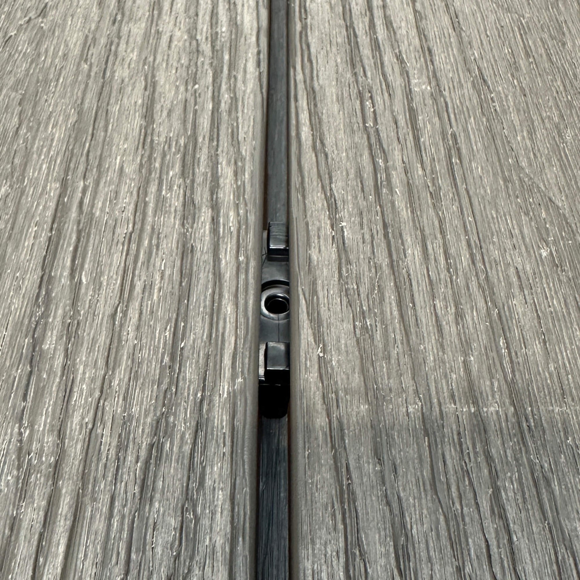 A Black Decking Clip in situ on a decking patio background.
