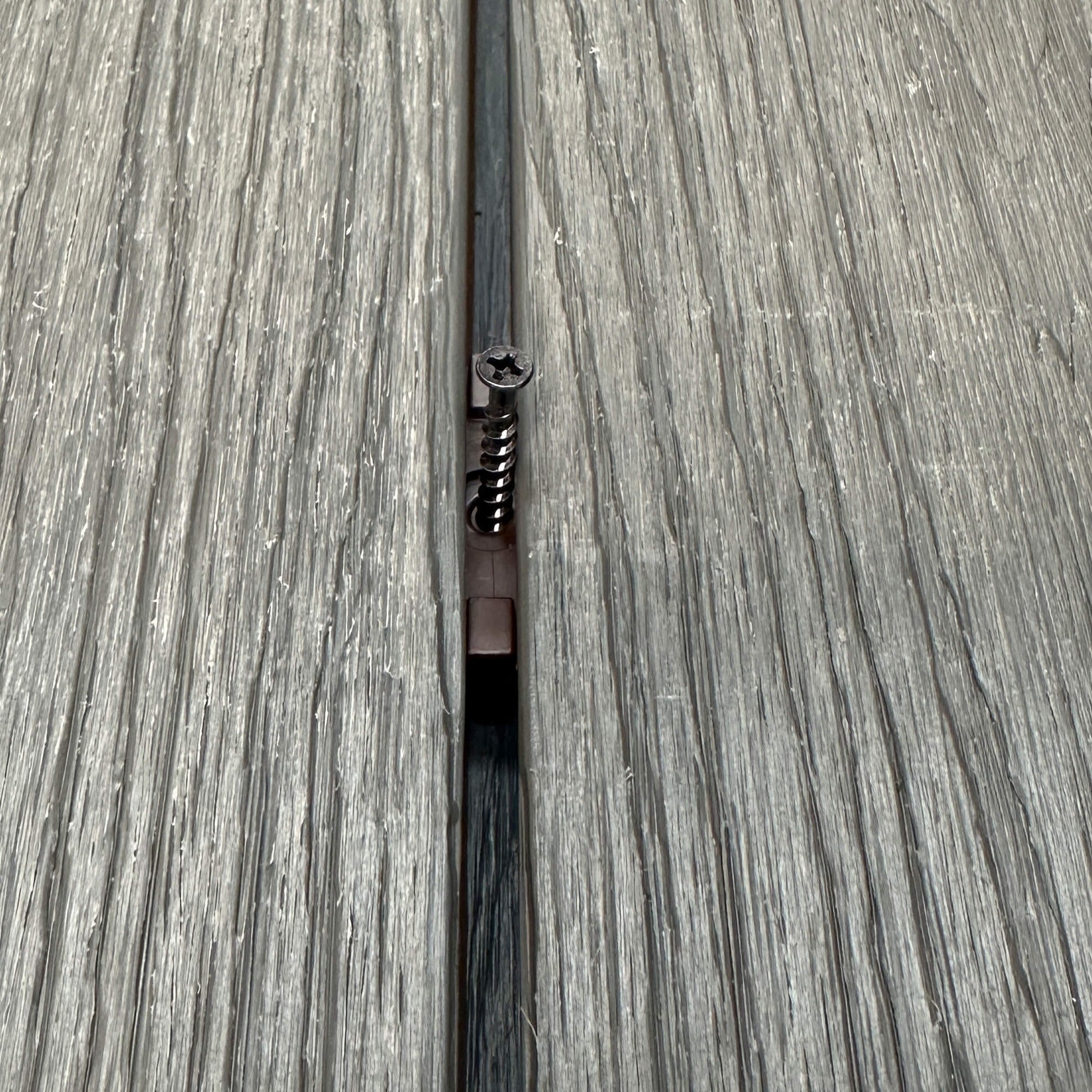 A Brown Decking Clip & Screw in situ on a decking patio background.