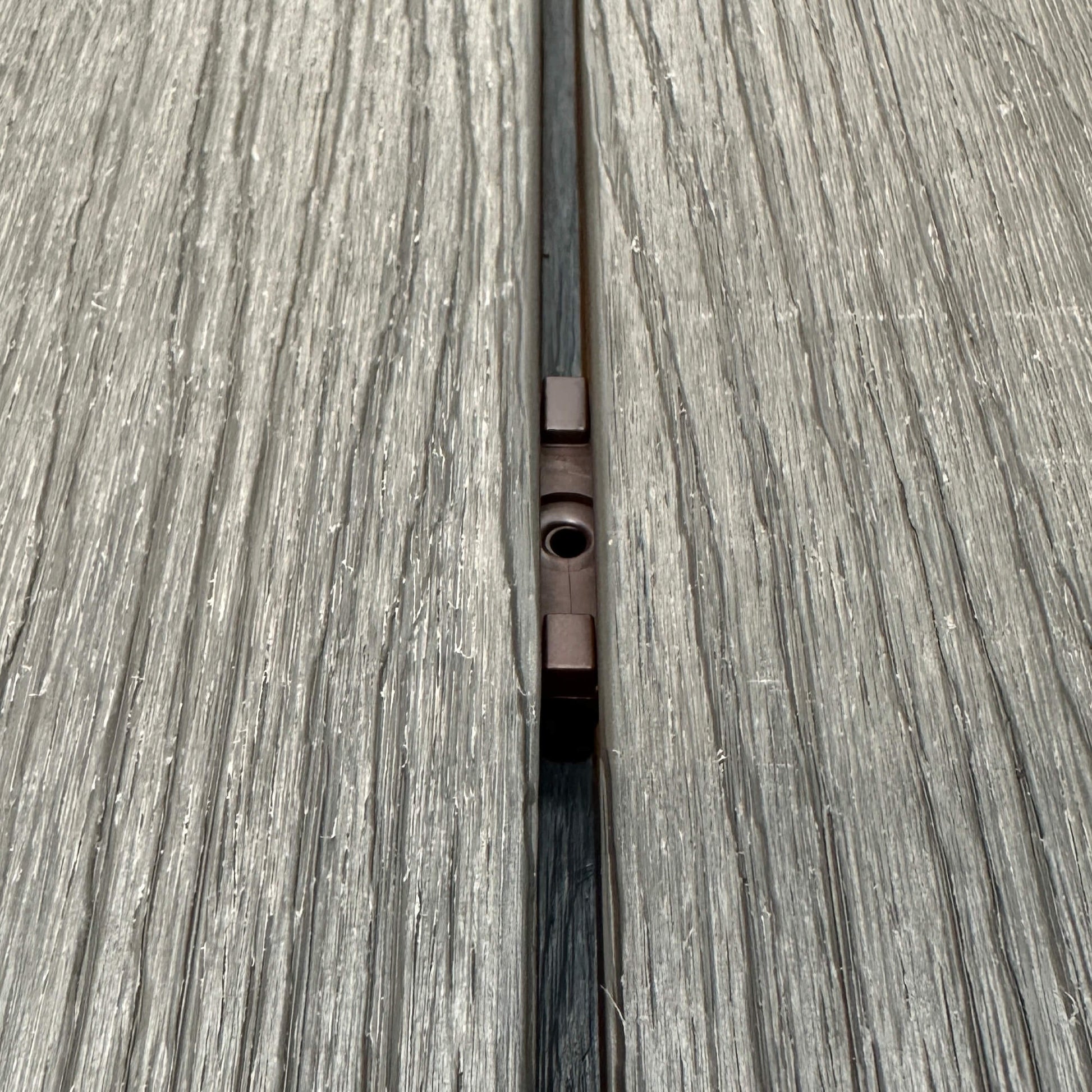 A Brown Decking Clip in situ on a decking patio background.
