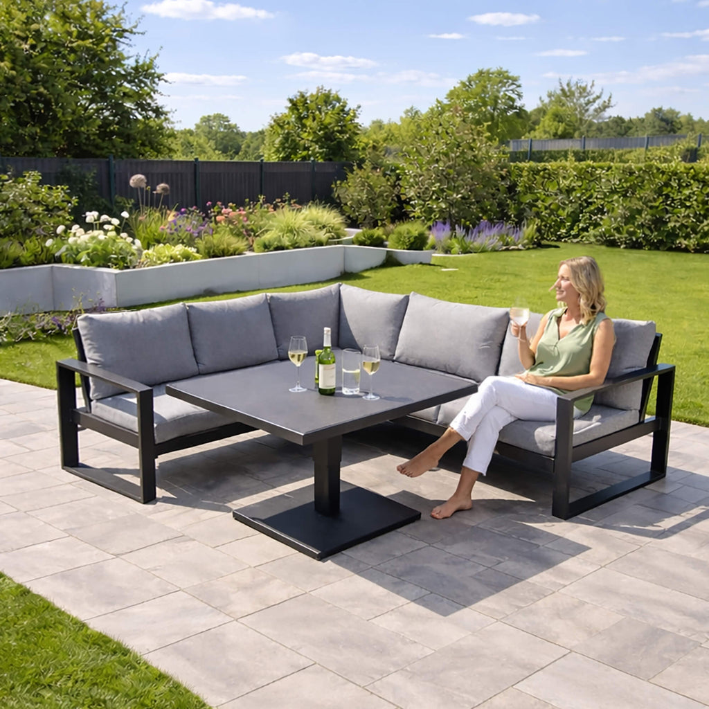 Woman sitting on a Como dark grey outdoor corner set, enjoying a drink in a garden setting.