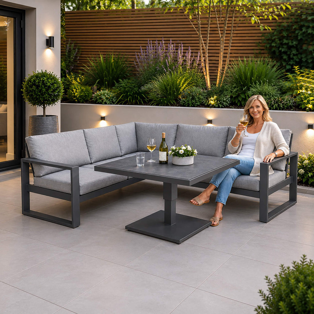 A woman sitting on a Como dark grey outdoor corner set in a patio setting.