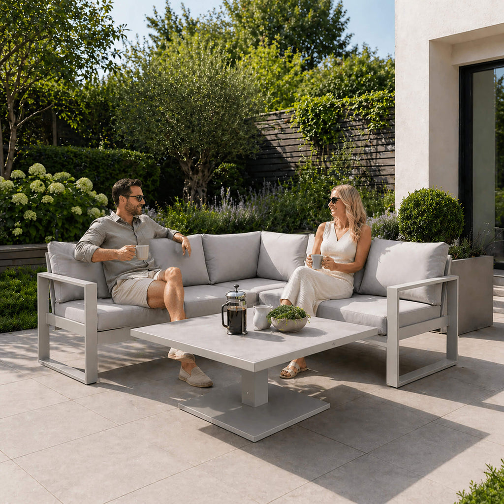 Two people sitting on a Como stone outdoor furniture corner set in a garden setting.