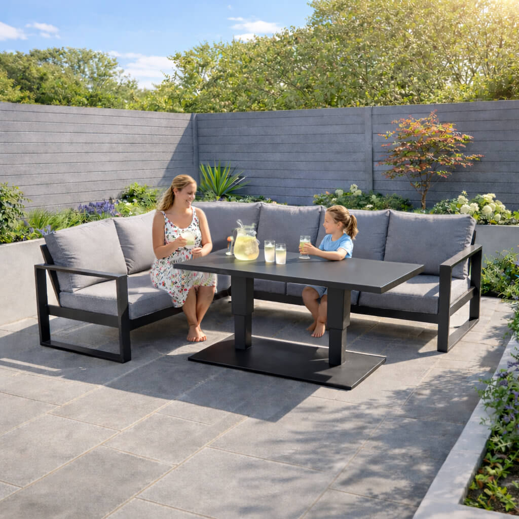 Mother and daughter sitting and relaxing on a Como dark grey L-shaped outdoor furniture corner set in a patio setting.