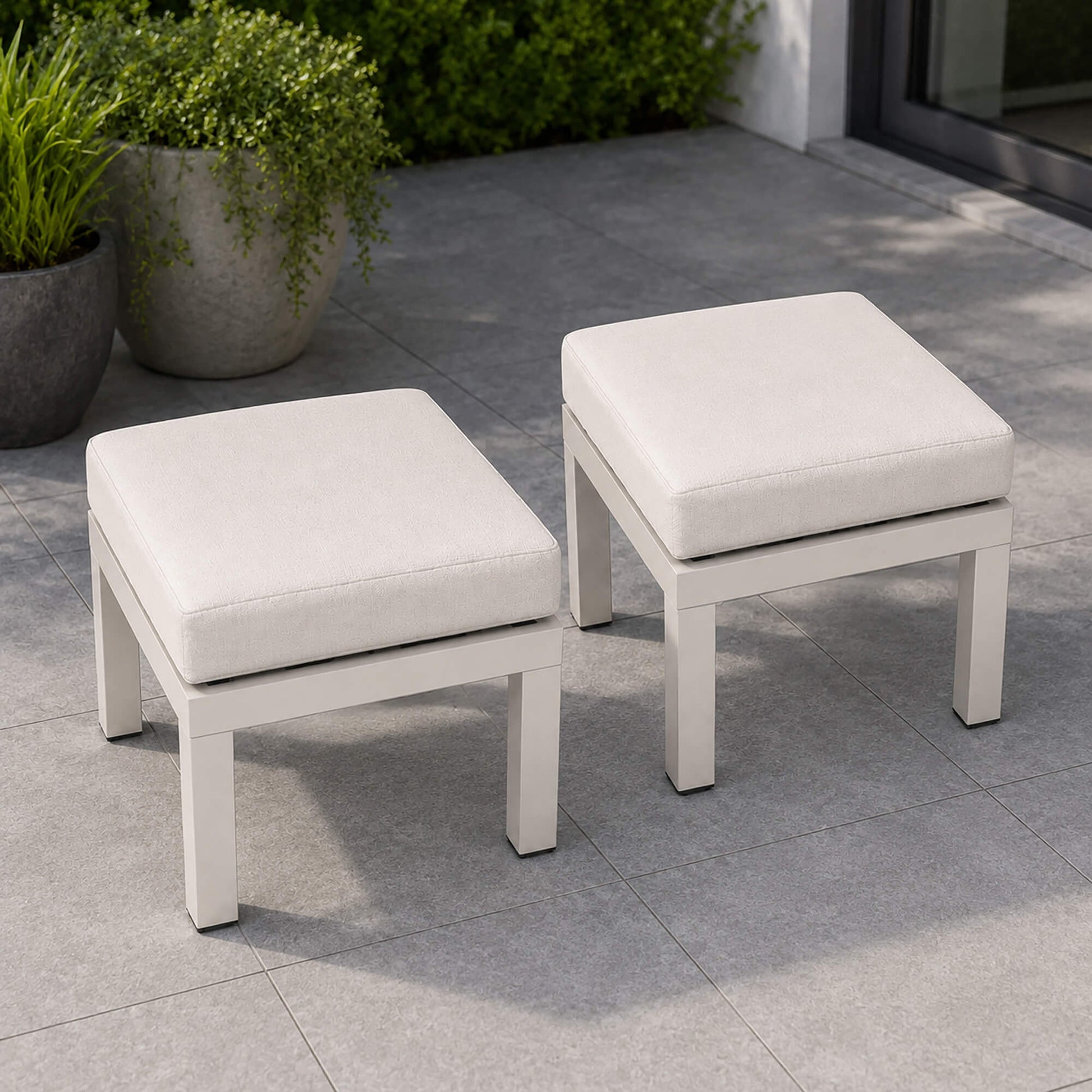 Como foot stool set with cushioned seats on a tiled patio with potted plants in the background.