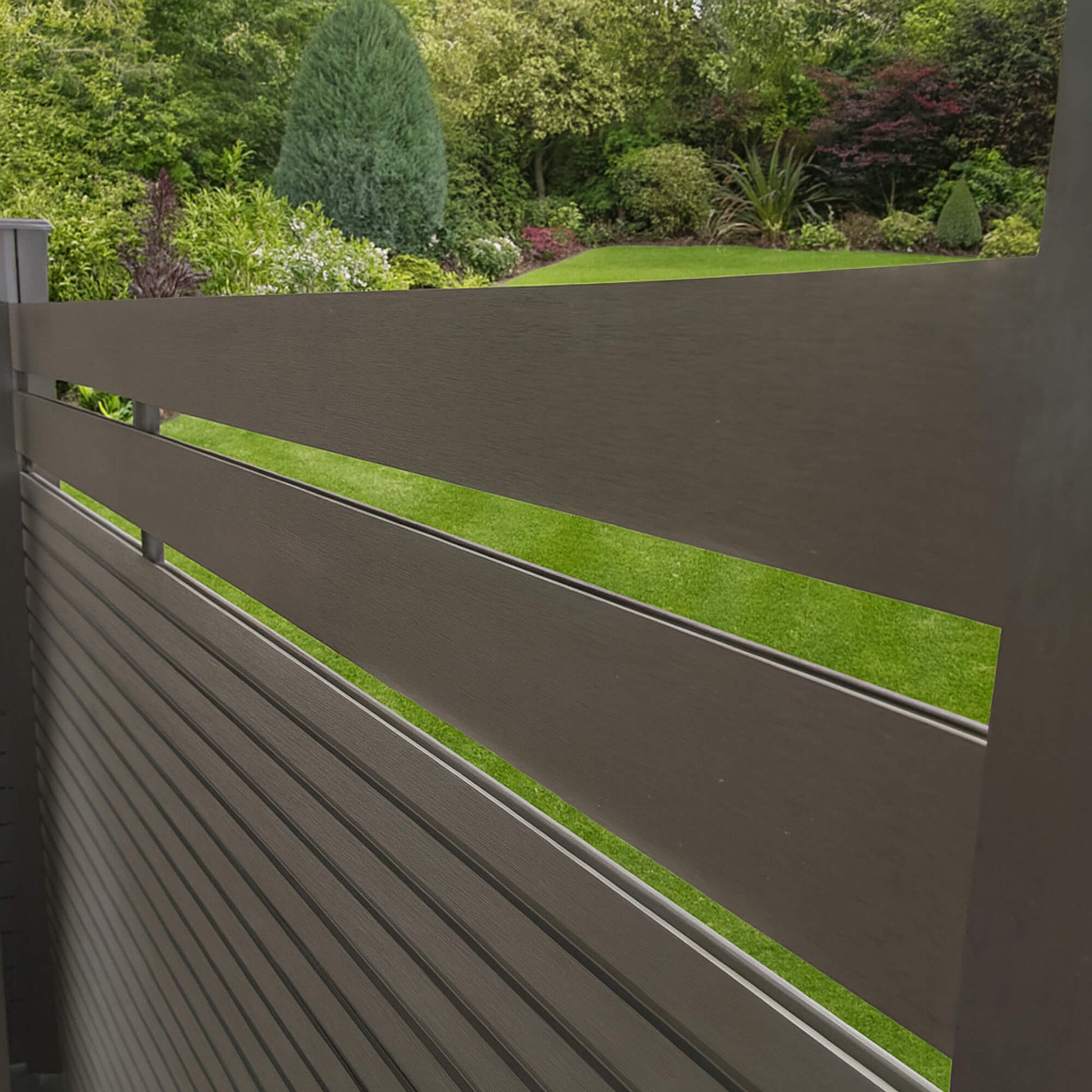 Angled view of a Charcoal Composite Fence Slat on top of a dark grey composite slatted fence in a garden setting.