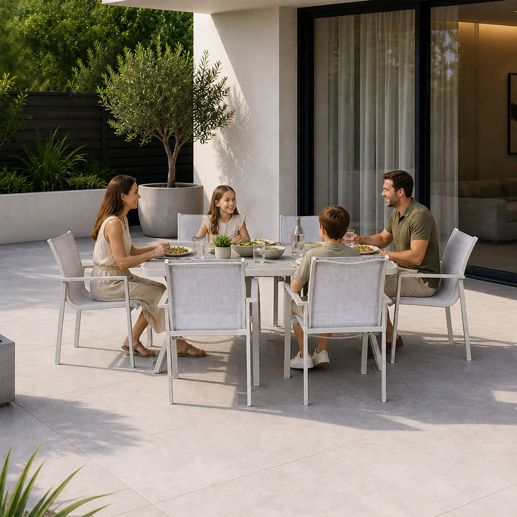 A family of four sits at a Garda Stone Outdoor Dining Furniture Set with four matching outdoor mesh chairs on a modern patio. 
