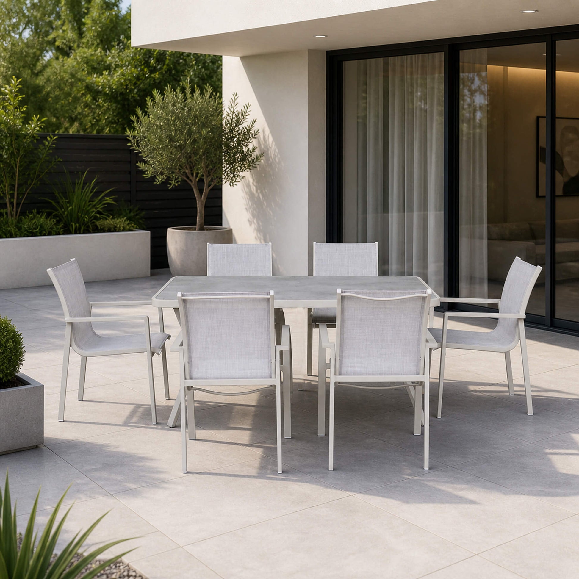Garda Stone Outdoor Dining Furniture Set with table and chairs on a patio in front of a modern house.